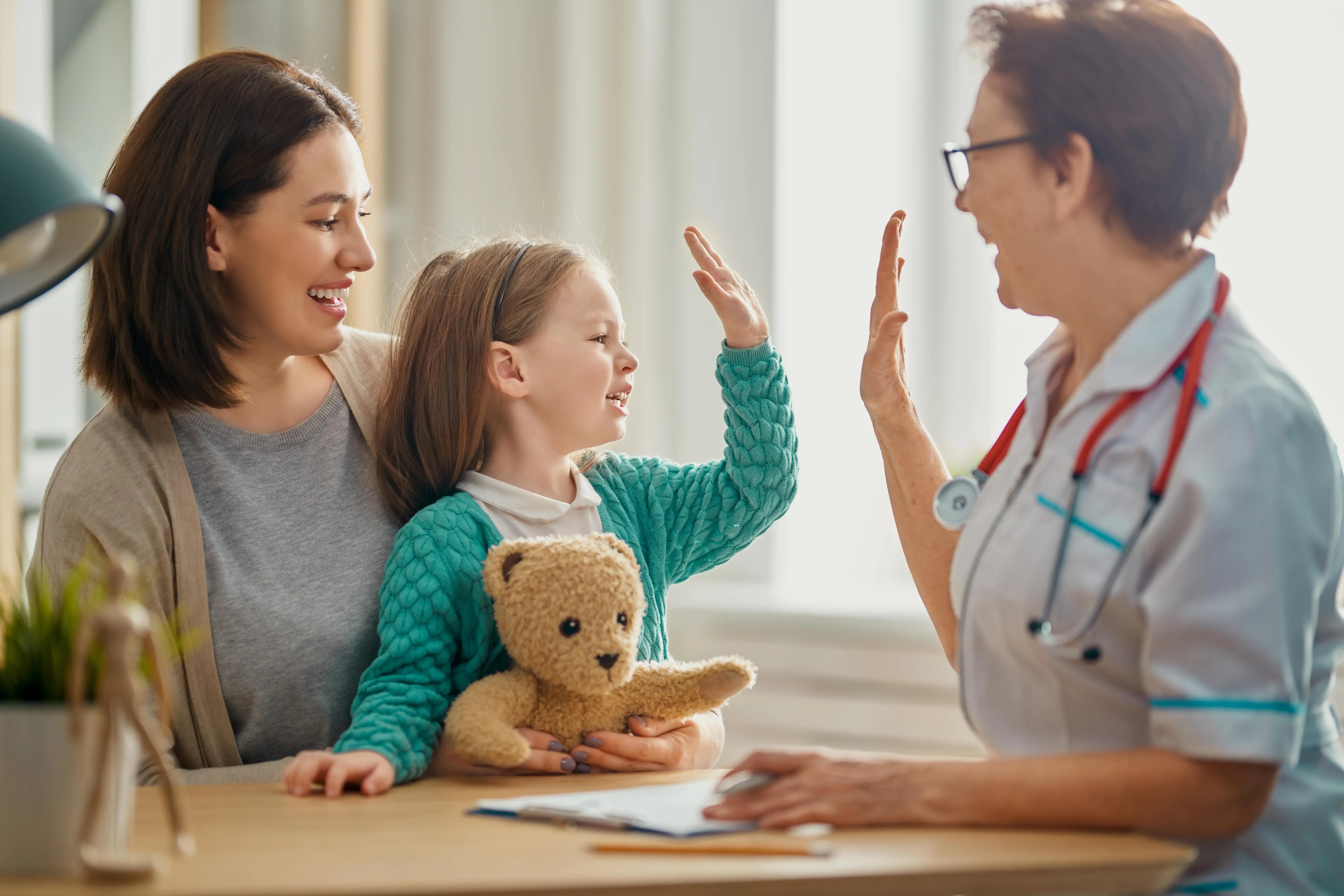 Girl sitting on her mum's lap and high fiving a healthcare professional