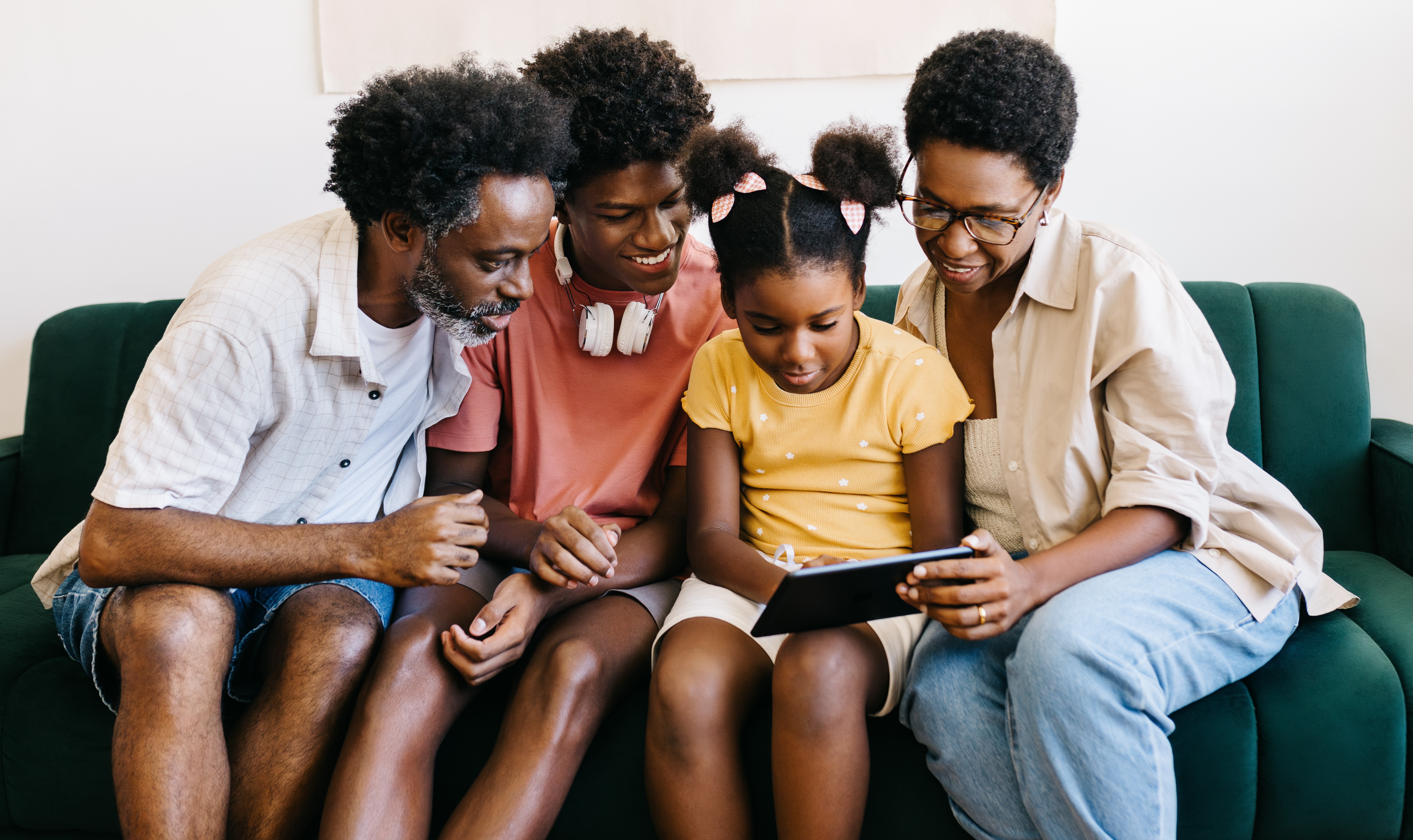 A parent and their two children are sat closely looking at a tablet.
