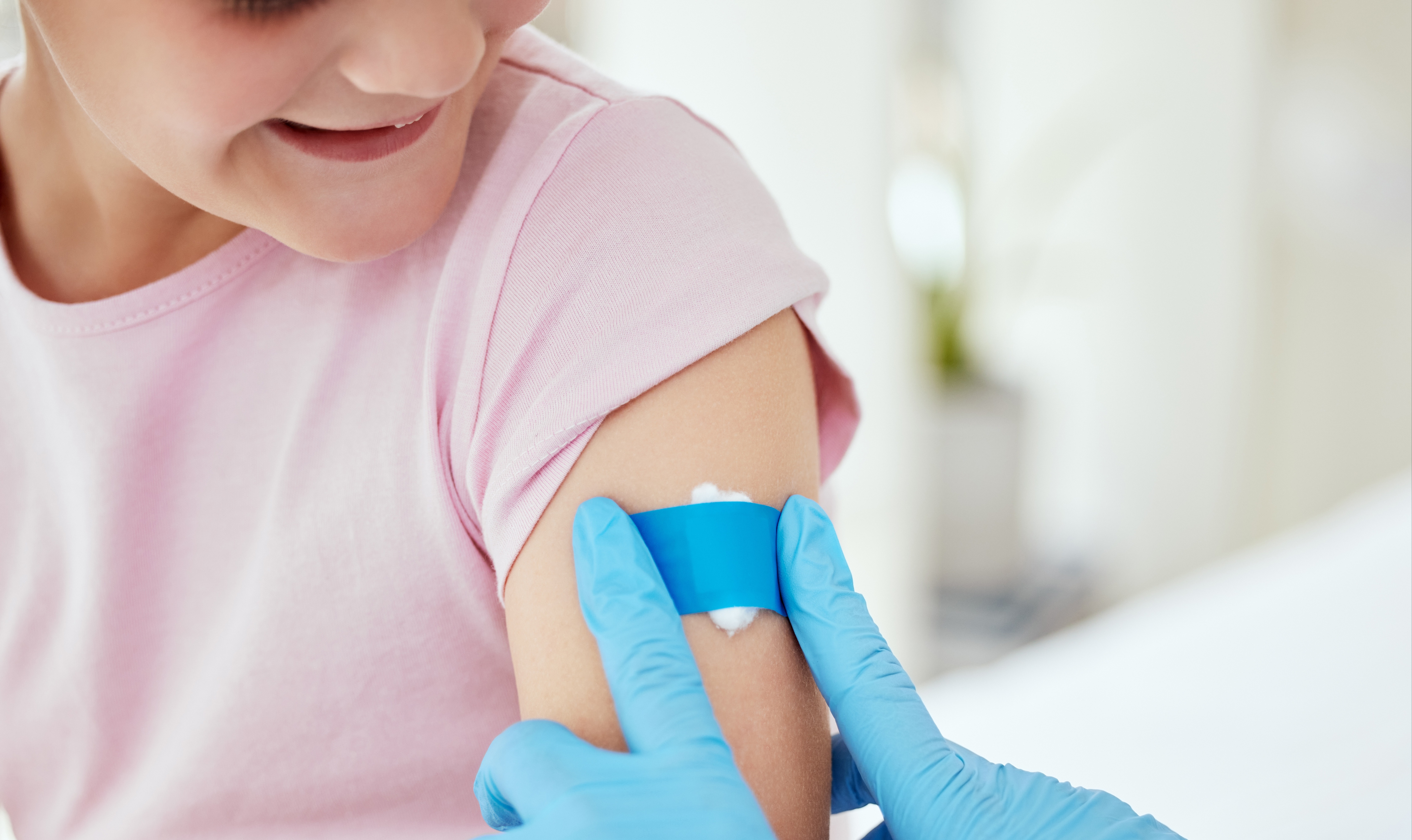 A clinician is placing cotton wool and a plaster over a child's arm.
