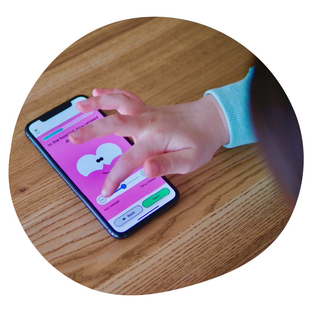 A child has a phone placed on the table, and is playing with the Little Journey app.